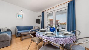 Un comedor con mesa de vidrio, cortinas azules y un sofá.