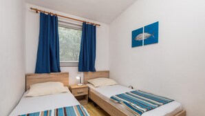 Un dormitorio con dos camas, una ventana con cortinas, una mesita de noche con una lámpara y dos cuadros en la pared.