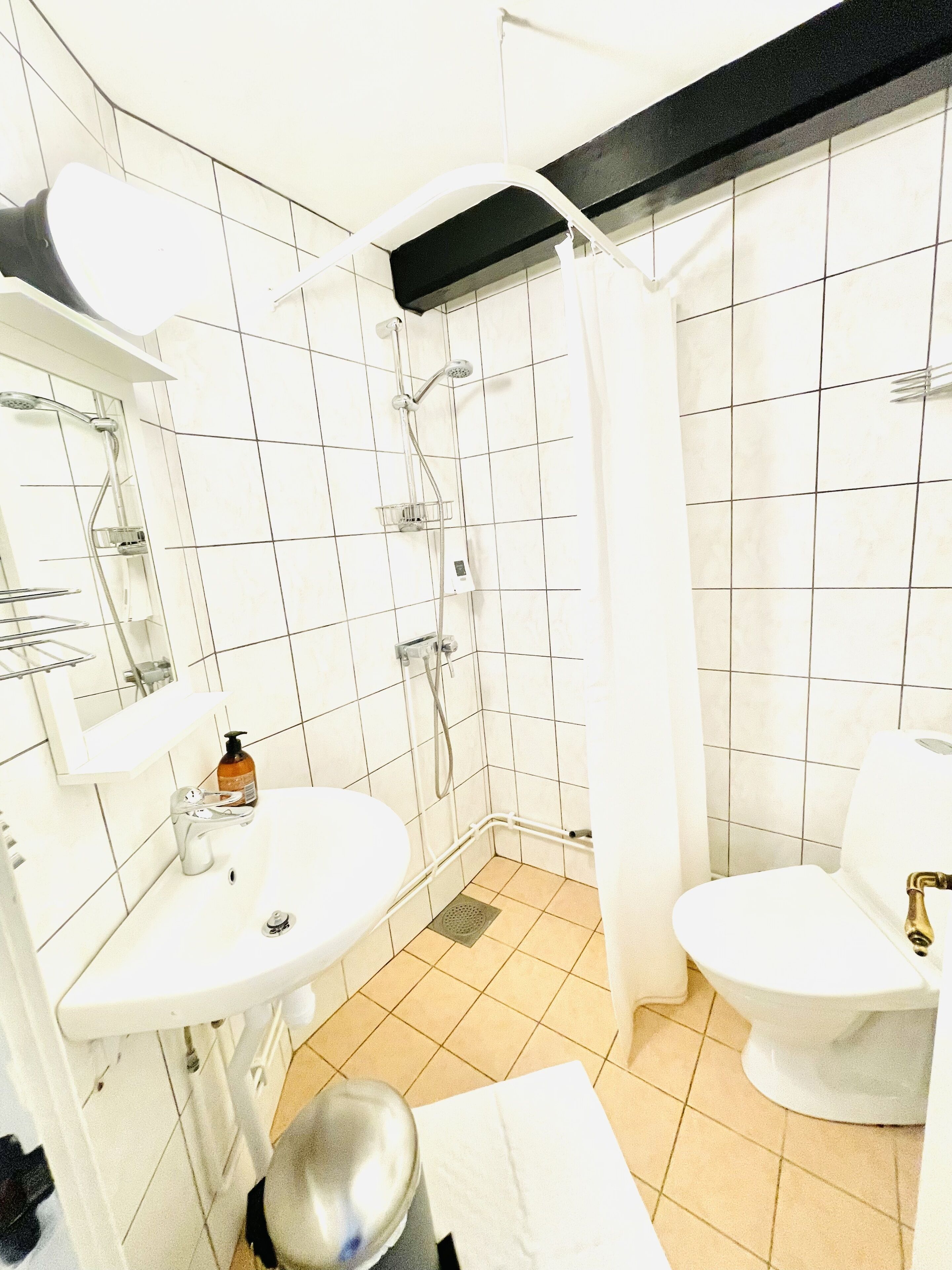 Une petite salle de bain avec des carreaux blancs, un lavabo, des toilettes et une douche.