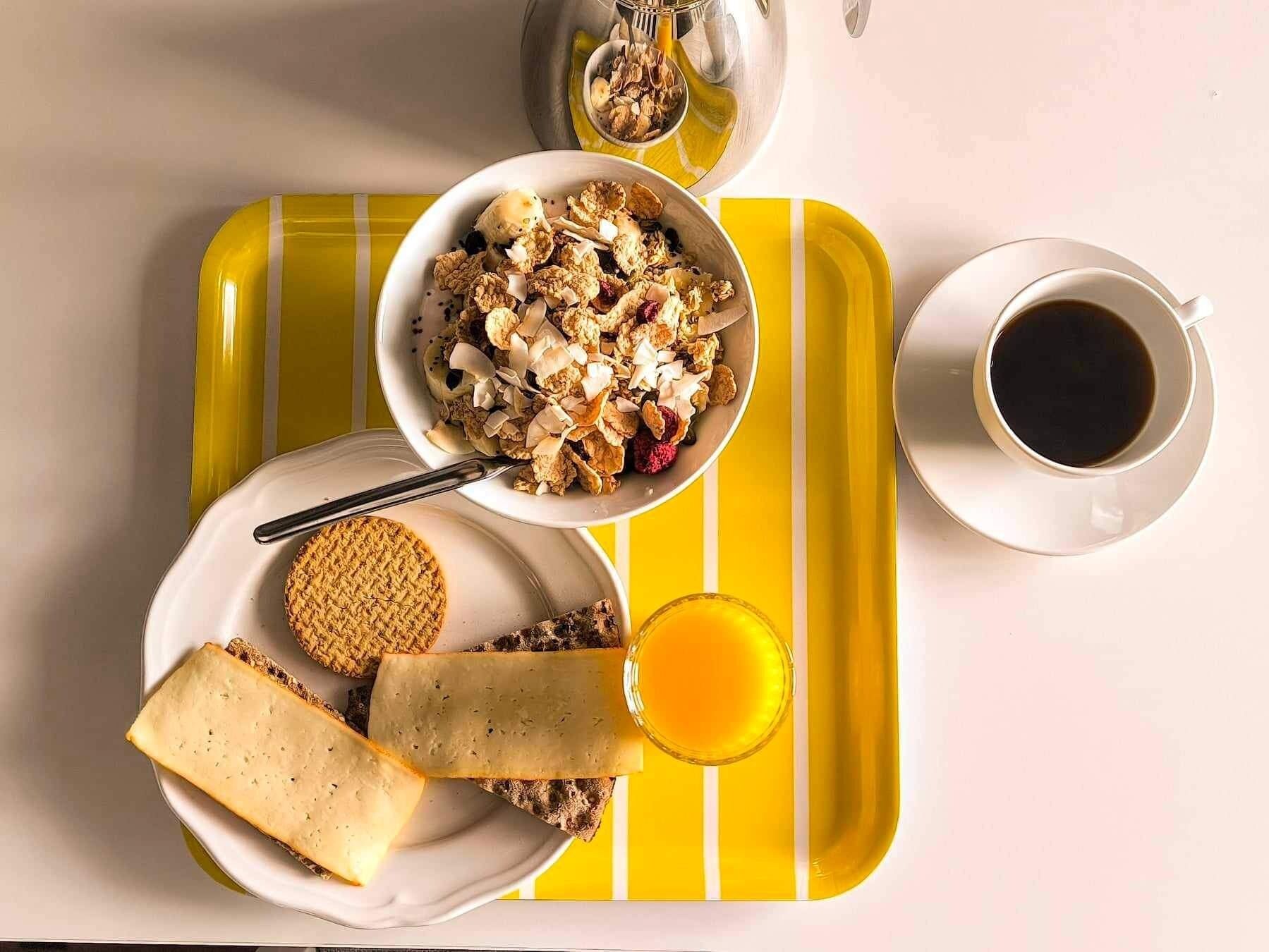 A breakfast tray with cereal, yogurt, cheese, and a glass of orange juice.