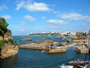 A coastal view with rocky formations, a lighthouse, and a marina with boats.