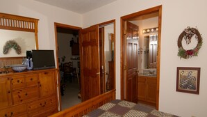 A bedroom with a wooden dresser, a bed with a patterned quilt, a mirror, and a bathroom visible through an open door.
