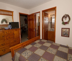 Un dormitorio con un aparador de madera, una cama con colcha estampada, un espejo y un baño visible a través de una puerta abierta.