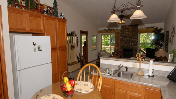 A kitchen with wooden cabinets, a white refrigerator, a dining table with placemats, and a fruit bowl.