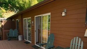A wooden deck with two Adirondack chairs and a small table, a sliding glass door, and a wall-mounted light fixture.