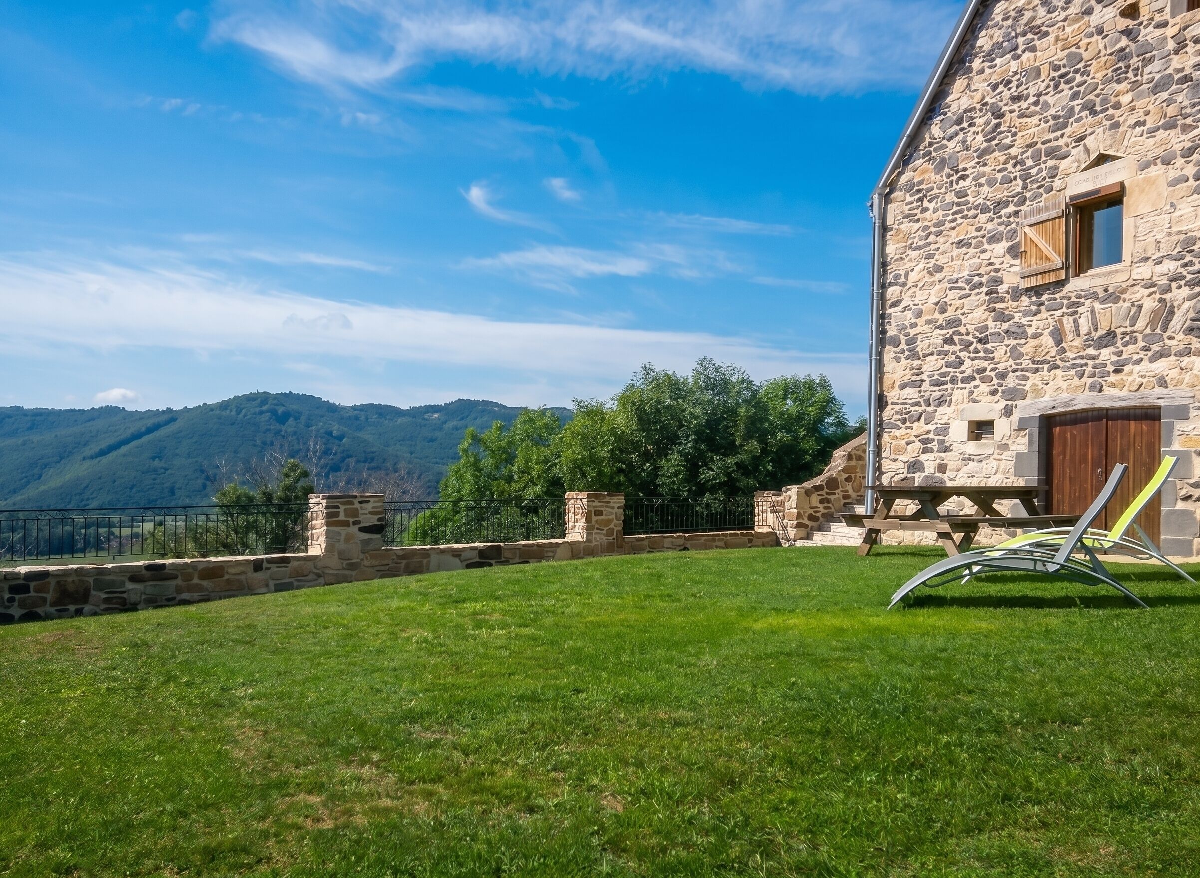 A stone building with a wooden door, a grassy lawn, and a view of mountains.