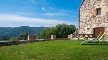 A stone building with a wooden door, a grassy lawn, and a view of mountains.