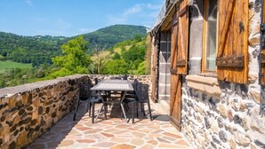 A stone patio with a table and chairs, a wooden door, and a view of green hills.