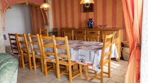 A dining area with wooden chairs and a table, a kitchen with wooden cabinets, and a hanging light fixture.