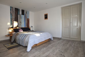 A bedroom with a wooden bed, a nightstand, a wall-mounted lamp, a door, and a patterned rug.