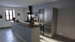 A modern kitchen with a central island, stainless steel appliances, and a window providing natural light. - THE 46, located on the edge of the D265, without neighborhood, surrounded by meadows and forests (Saint-Sauveur-la-Sagne)