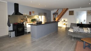 A spacious living area with a kitchen, a grey sofa, a wooden staircase, and a small dining table. - THE 46, located on the edge of the D265, without neighborhood, surrounded by meadows and forests (Saint-Sauveur-la-Sagne)