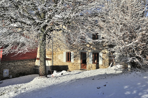 A stone building with a red door and windows, surrounded by snow-covered branches.