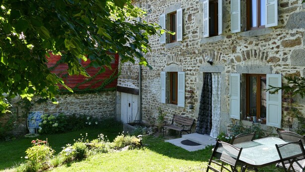 A stone building with white shutters, a bench, and a table with chairs in the garden area. - THE 46, located on the edge of the D265, without neighborhood, surrounded by meadows and forests (Saint-Sauveur-la-Sagne)