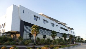 A modern building with a flat roof, large windows, and a landscaped area with palm trees and shrubs. - Architect house with pool near the sea (Sète), WiFi, Climate, Clévacances 4Clés (Balaruc-les-Bains)