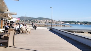 A wooden pier with outdoor seating, a view of the sea, and a distant town. - Architect house with pool near the sea (Sète), WiFi, Climate, Clévacances 4Clés (Balaruc-les-Bains)