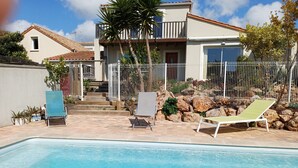 A swimming pool with lounge chairs, a stone wall, and a two-story house with a balcony. - Architect house with pool near the sea (Sète), WiFi, Climate, Clévacances 4Clés (Balaruc-les-Bains)