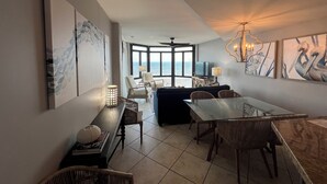 Amplia sala de estar con un ventanal grande con vista al mar, una mesa de comedor con sillas, un sofá y un televisor.
