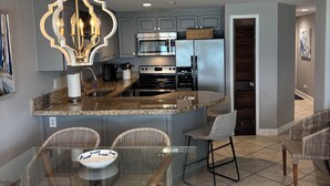 Una cocina moderna con una isla central, electrodomésticos de acero inoxidable y sillas de mimbre alrededor de una mesa de vidrio.