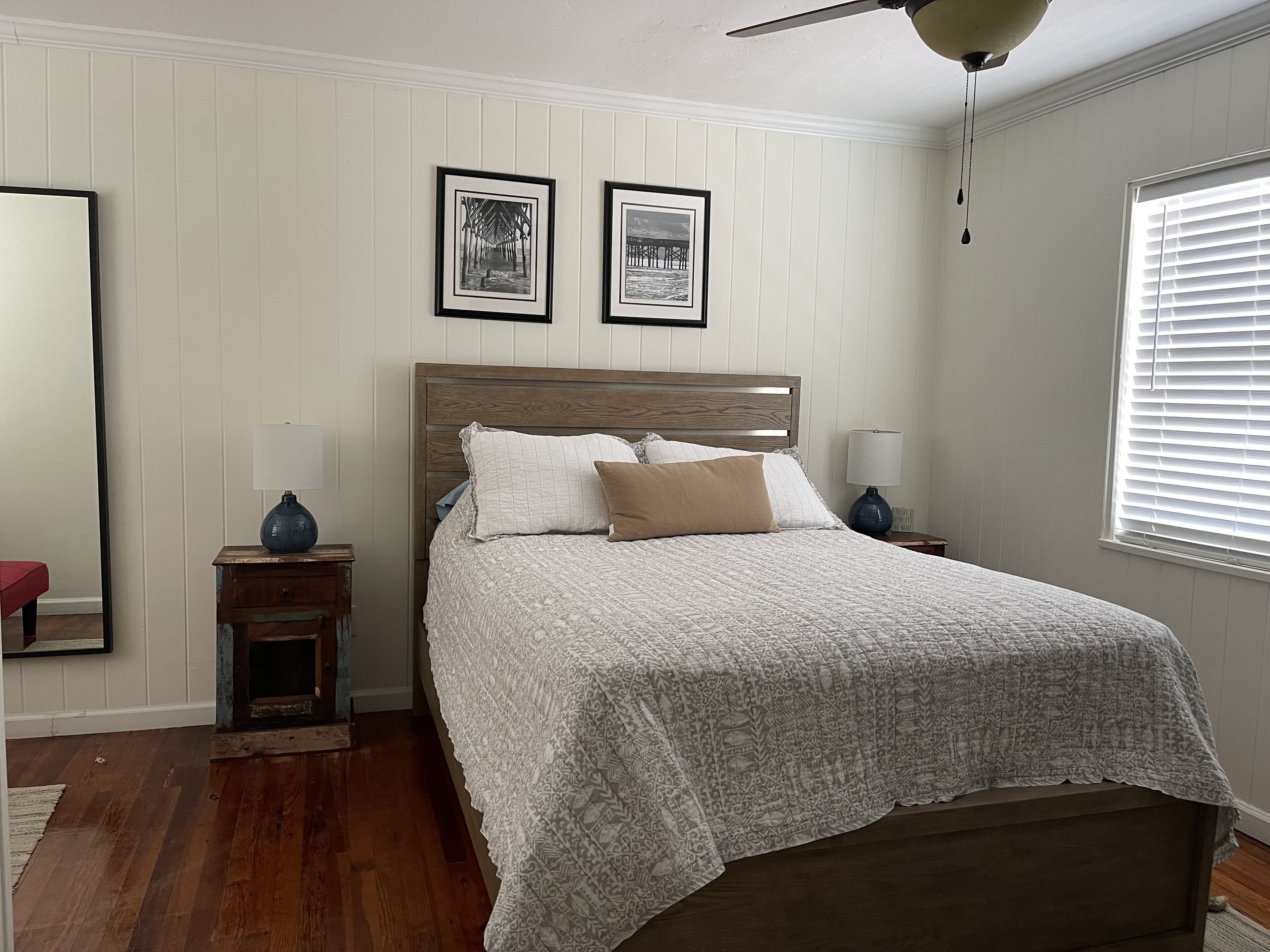 A bedroom with a wooden headboard, a patterned bedspread, two bedside lamps, and two framed pictures on the wall.