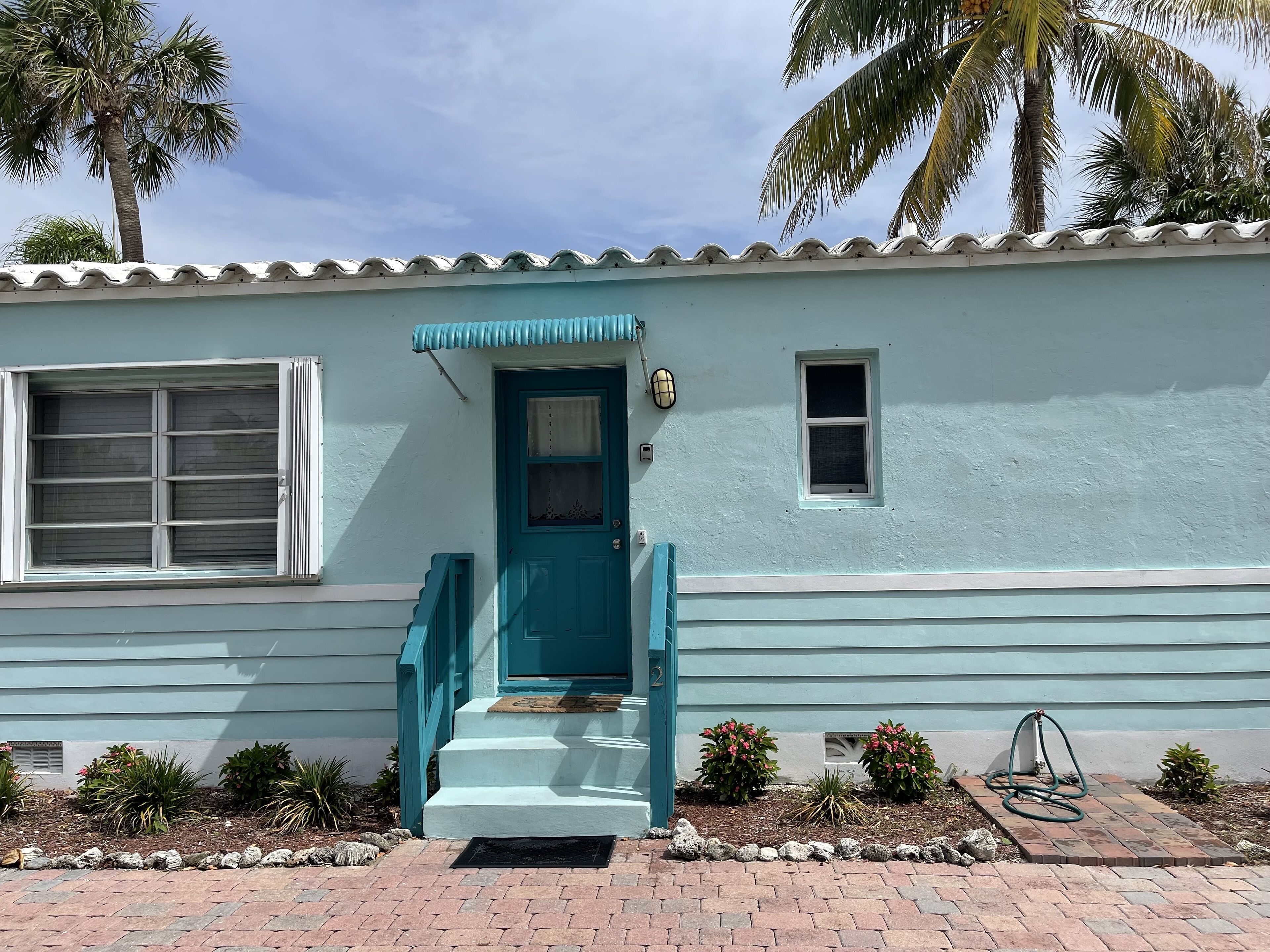 Una casa con una puerta azul verdosa, una ventana y un balconcito.