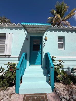 A turquoise house with a blue door, white shutters, and a small window.