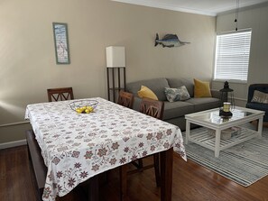 A dining area with a table set for four, a sofa, a lamp, and a wall-mounted fish decoration.