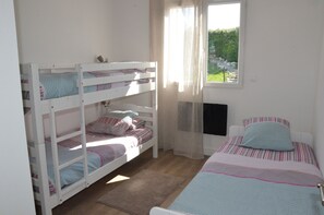 A bunk bed room with a window, a single bed, and a view of greenery outside.