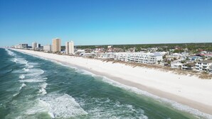 Paesaggio urbano costiero con spiaggia sabbiosa, onde dell'oceano e diversi edifici, tra cui hotel e abitazioni.