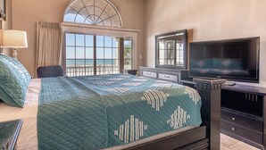 Una camera d'albergo con un letto grande, una televisione, un comò e una finestra vista oceano.