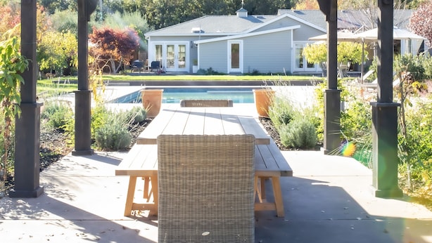 Un patio techado con mesa de billar, mobiliario exterior y vista hacia una casa al fondo.