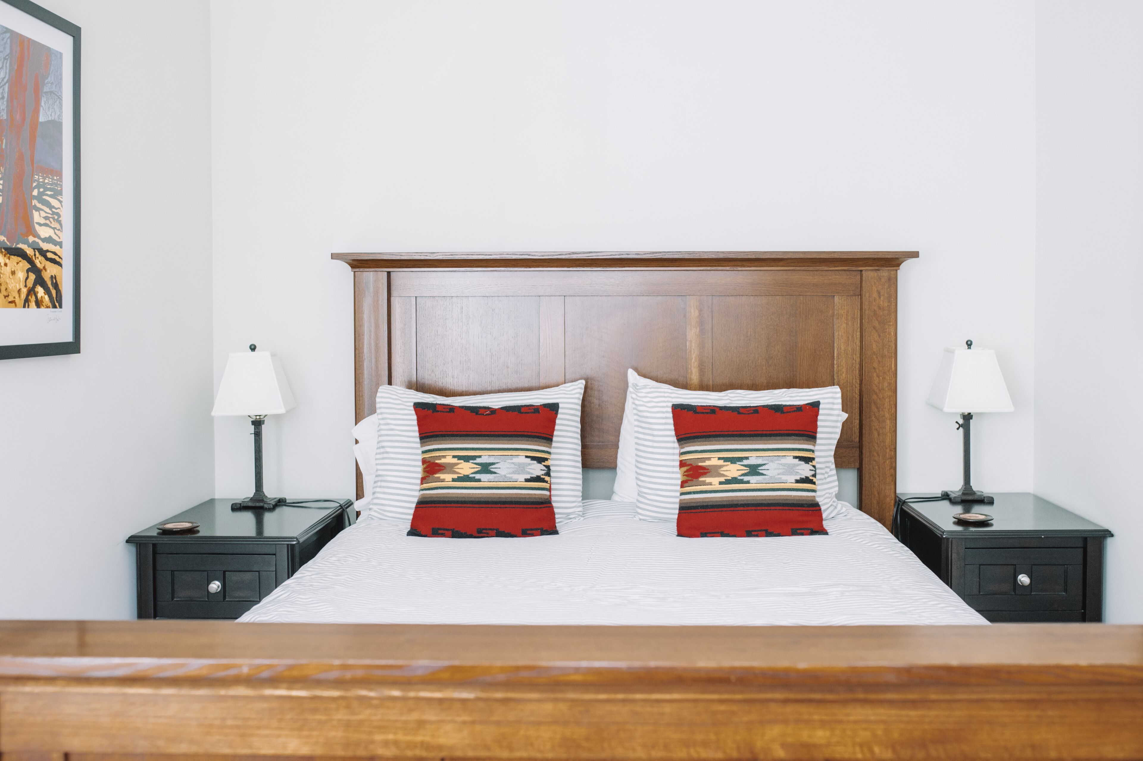 A neatly made bed with two pillows, a wooden headboard, and two bedside tables with lamps.