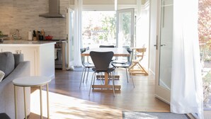 Una cocina moderna con una isla central, un comedor con mesa y sillas, y vistas a un espacio exterior por una puerta de vidrio.