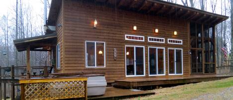 A wooden cabin with a deck, large windows, and a covered porch.