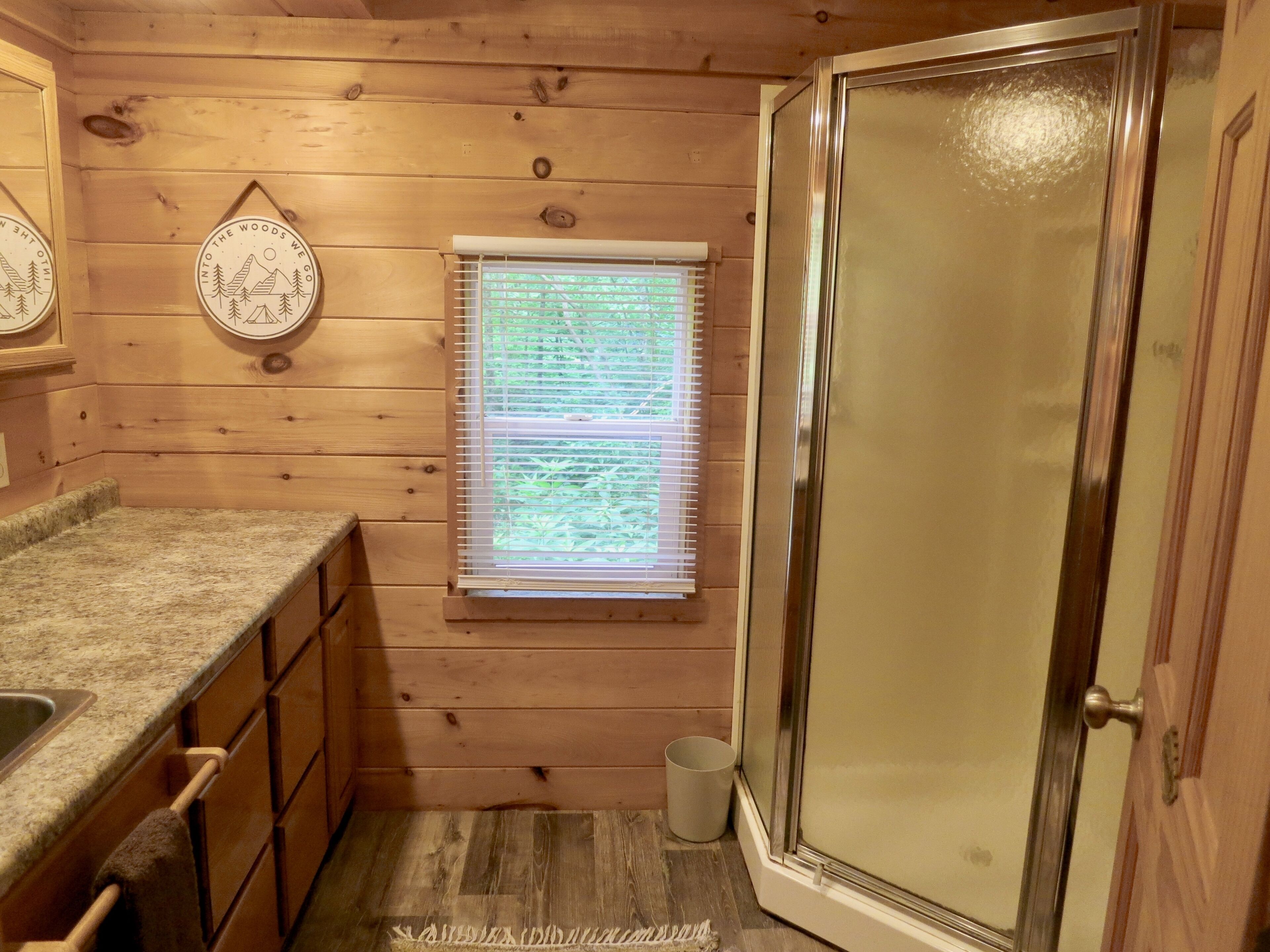 Interior de una cabaña de madera con cocina, una ventana con persianas y una puerta.