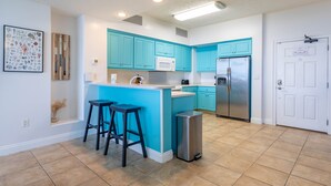 Une cuisine moderne avec des meubles de couleur turquoise, un réfrigérateur en acier inoxydable et un petit îlot central doté de tabourets.