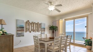 Un coin repas avec une table et des chaises, un ventilateur de plafond et une vue sur l’océan grâce à une porte-fenêtre coulissante.