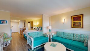 A hotel room with a bed, two sofas, a small table, and a chair. There is a door leading to another room and a bathroom. - Studio Condo in Town, Near Beach, Shared Pool and Hot Tub (Port Aransas)