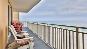A balcony with two Adirondack chairs and a table, overlooking a beach.