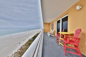 Un balcón con vista a la playa, con sillas rojas y amarillas y una pequeña mesa.