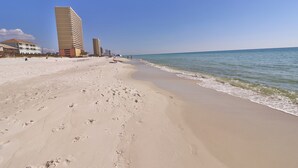 A beach with footprints leading to the water, a tall hotel, and a clear sky.