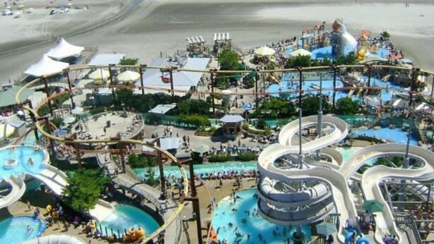Een waterpark met glijbanen en zwembaden, omgeven door een strand en uitzicht op de oceaan.