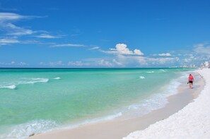 A beach with clear turquoise water and a person walking along the shore.
