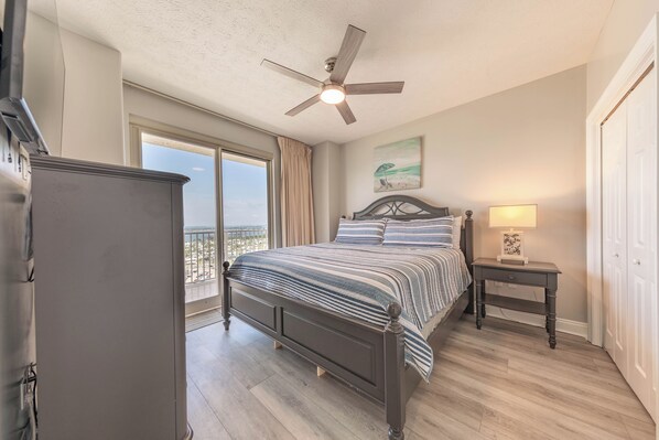 Quarto com cama, ventilador de teto, mesa de cabeceira e vista para o exterior.