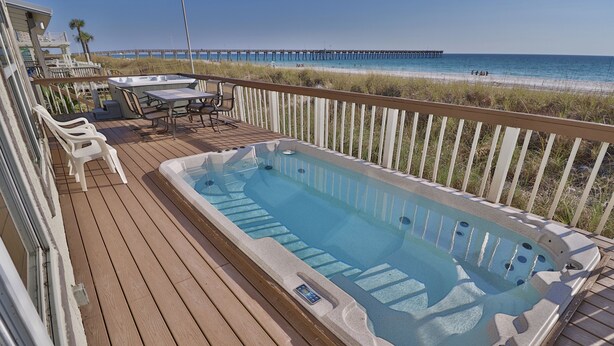 Una terraza de madera con un jacuzzi, mobiliario exterior y vistas a la playa y el muelle.