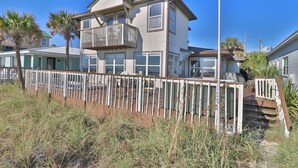 Una casa de dos pisos con balcón, rodeada de hierba alta y palmeras.