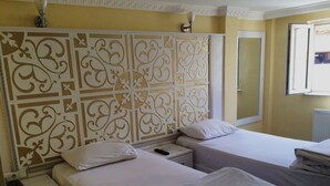 Habitación de hotel con dos camas, un cabecero decorativo, una mesita de noche con control remoto y una ventana con vistas.