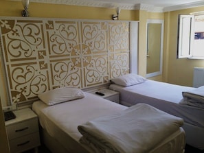 Classic hotel room with two single beds, a nightstand, and a window offering a view of the outside.