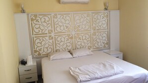 Una cama bien hecha con sábanas y almohadas blancas, una mesita de noche con una lámpara y un cabecero decorativo con diseños intrincados.