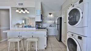 A kitchen with a central island, two bar stools, a double-door refrigerator, and stacked front-loading washing machines. - Summit 1 BR SLEEPS 5  ***BEACH CHAIRS INCLUDED*** (Panama City Beach)